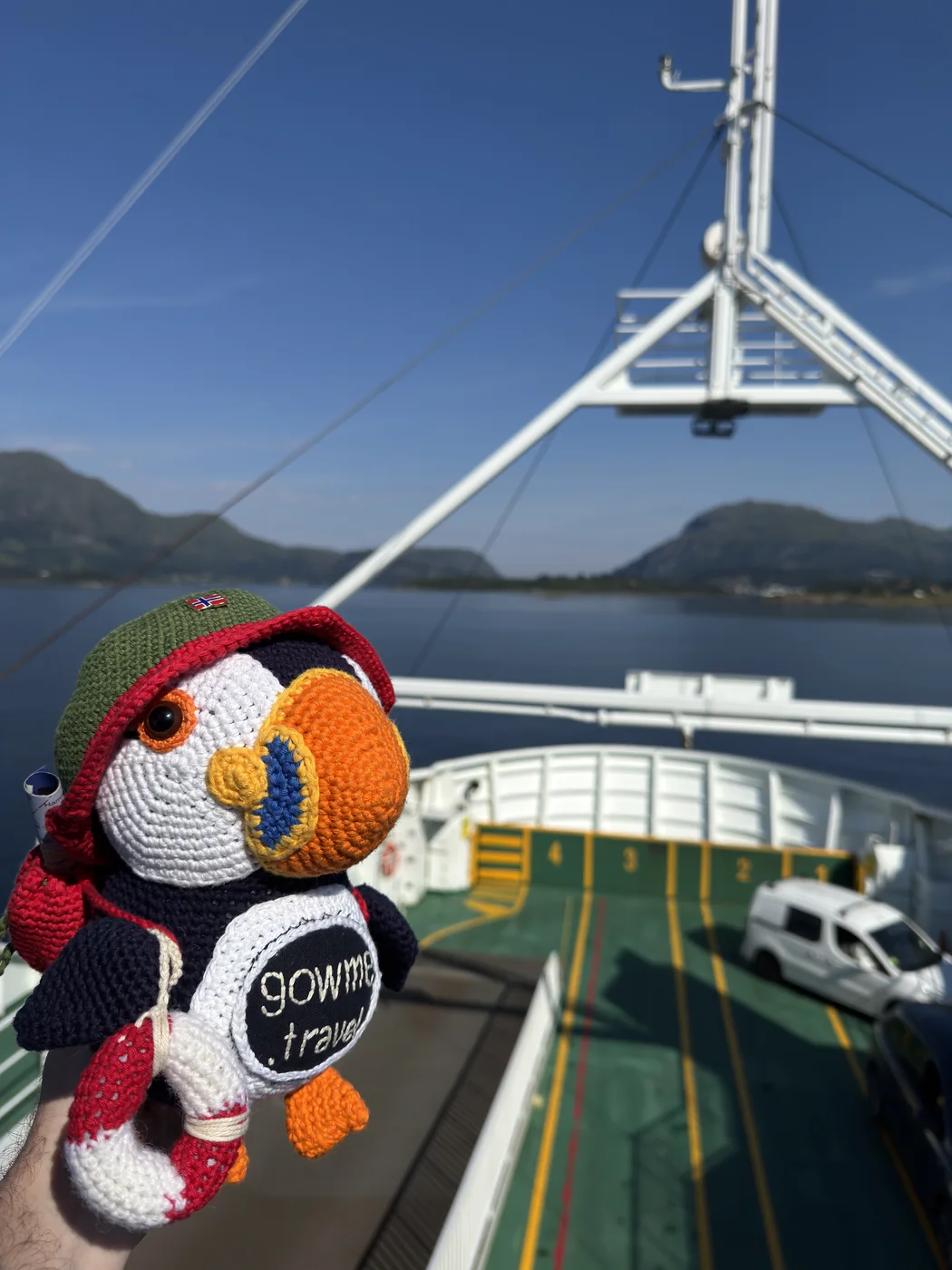 Fluffy the gowme.travel puffin on the deck of a Norwegian car ferry, with mountains and a fjord behind