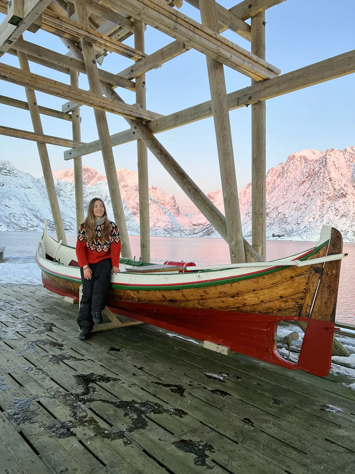 A Gowme.travel author beside a traditional wooden Nordland boat on the Hamnøy wharf, with the snowy Lofoten mountains behind