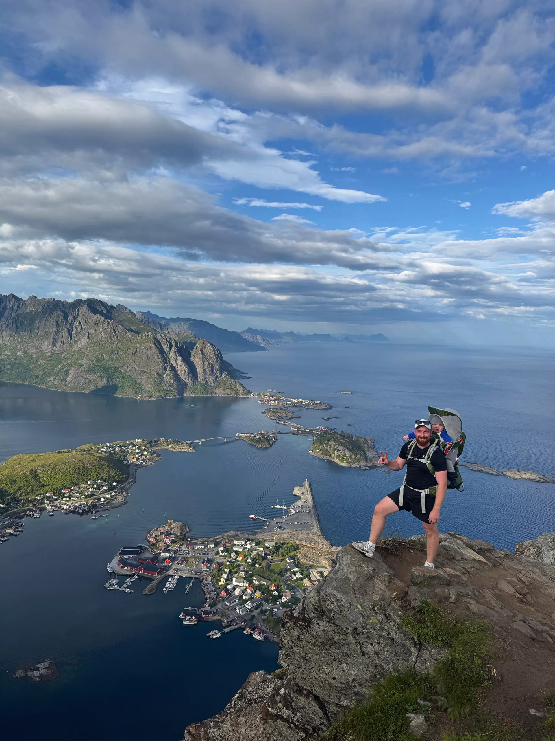 A Gowme.travel author with our child in a carrier backpack at the Reinebringen viewpoint, high above Reine, Lofoten
