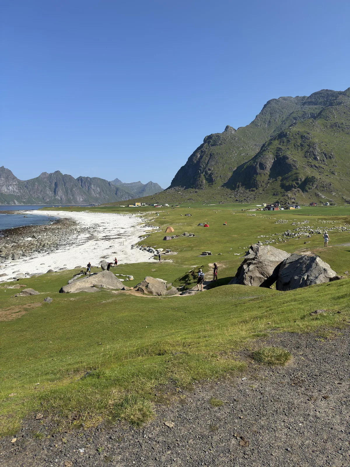 Our photo of Uttakleiv Beach — white sand, big shore boulders, tents at the camping area and the steep Lofoten mountains behind